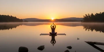 Serene sunrise over lake with person meditating, embodying mindful morning habits.